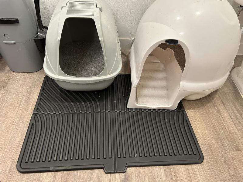 A rabbit litter box sitting on a waterproof washable mat in a living room corner, with a hay feeder attached above