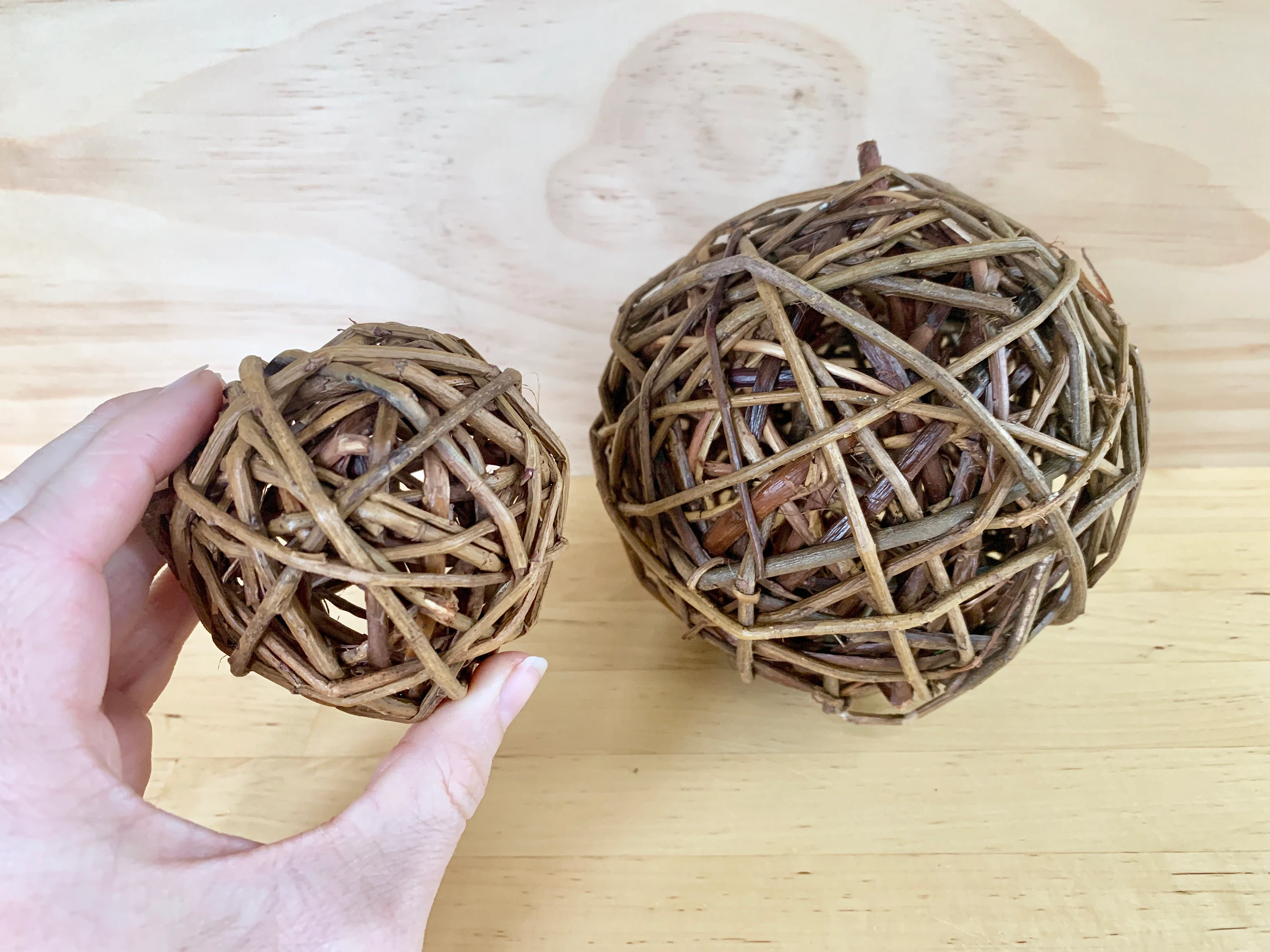 A small rabbit chewing on a plain woven willow ball inside a tidy indoor enclosure