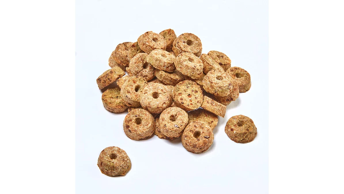 Small green-speckled hay biscuits on a parchment-lined baking sheet with fresh carrot tops beside the tray